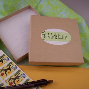 May include: A brown cardboard box with a white label that says "A Smile Built In". The box is open and has white tissue paper inside. The box is sitting on a yellow surface.