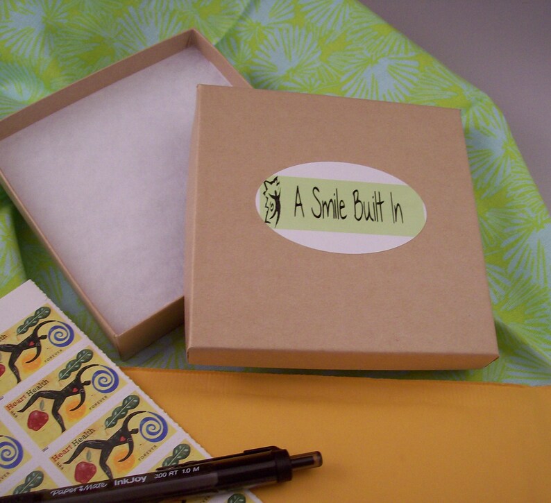 May include: A brown cardboard box with a white label that says "A Smile Built In". The box is open and has white tissue paper inside. The box is sitting on a yellow surface.