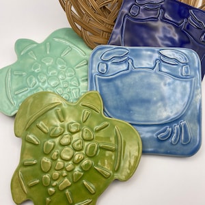 May include: Four ceramic tiles with a sea life theme. One tile is a light green turtle, one is a light blue turtle, one is a dark blue turtle, and one is a light green turtle with a textured shell.