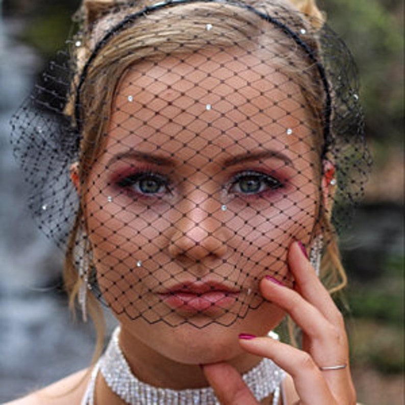 May include: A black birdcage veil with rhinestones, worn over a woman's face. The veil is made of fine netting and has a delicate, feminine look.