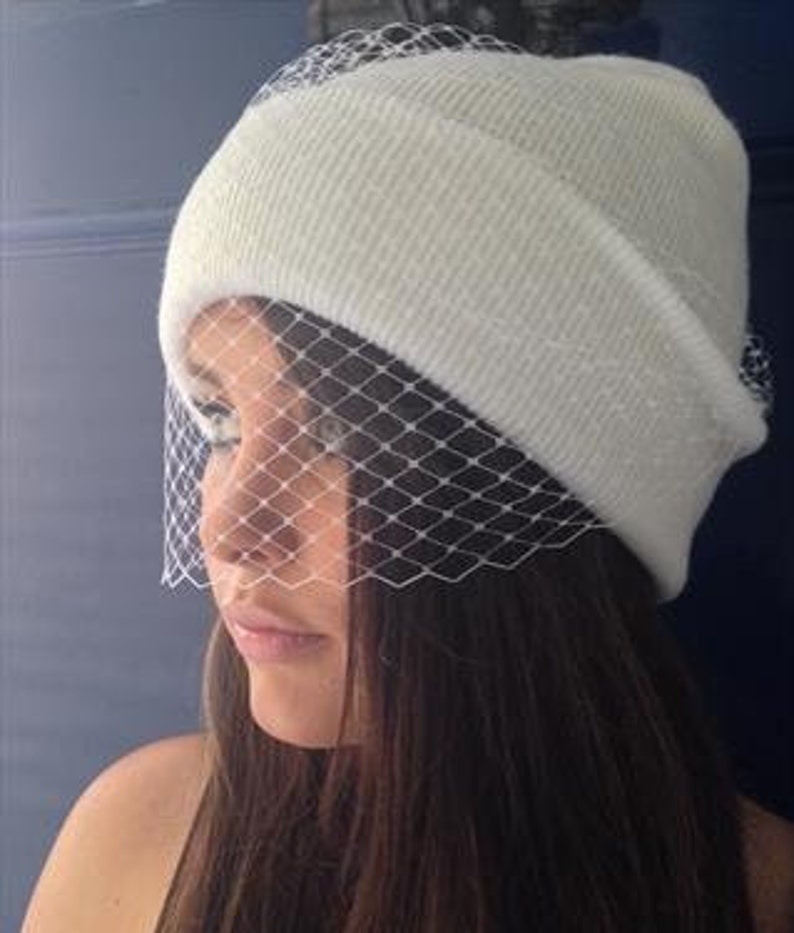 girl wearing pure white ribbed smooth beanie hat, folded cuff style and delicate vintage style fascinator veil to front to mask eyes