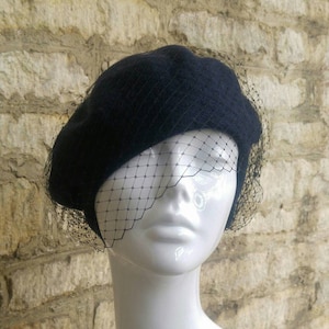 May include: A navy blue beret with a black tulle veil. The beret is made of felt and has a classic shape.