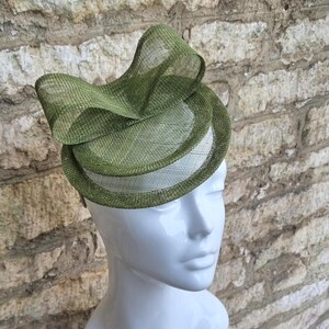 May include: A green fascinator hat with a large bow. The hat is made of a delicate, woven material and is perfect for a special occasion.