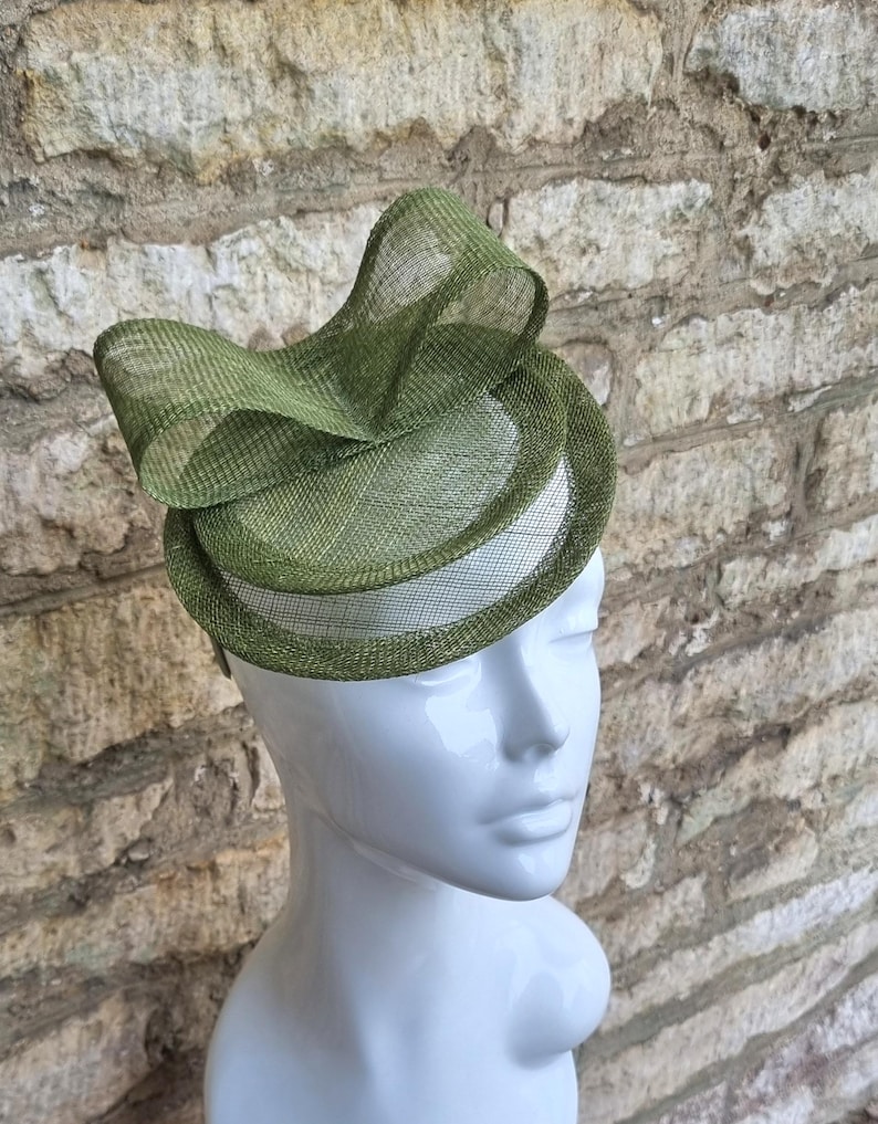 May include: A green fascinator hat with a large bow. The hat is made of a delicate, woven material and is perfect for a special occasion.