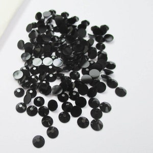May include: A large pile of black round rhinestones, scattered on a white surface.
