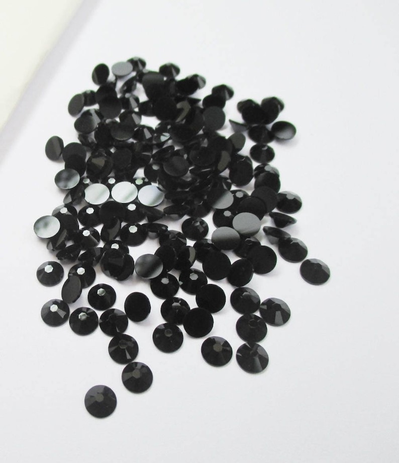 May include: A large pile of black round rhinestones, scattered on a white surface.