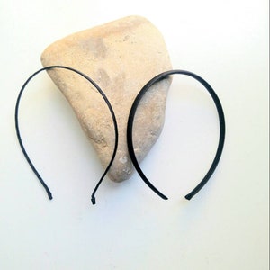 May include: Two black plastic headbands on a light brown rock. The headbands are thin and flexible.