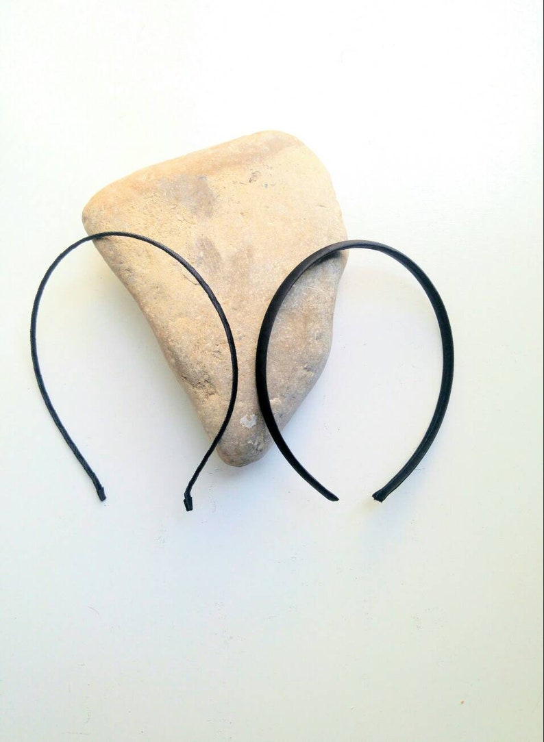 May include: Two black plastic headbands on a light brown rock. The headbands are thin and flexible.