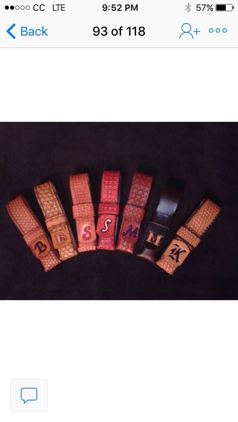 May include: A collection of leather belt keepers in various shades of brown and red, each embossed with a different letter. The letters are in different fonts and colors. The keepers are arranged on a dark background.