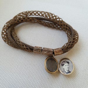 May include: A vintage brown hair bracelet with a woven design. The bracelet features ornate gold-toned metal clasps and a small locket with a portrait inside. The locket is open, revealing the image.
