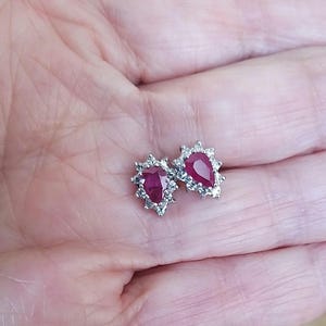 May include: A pair of pear-shaped ruby earrings with a halo of small clear stones.