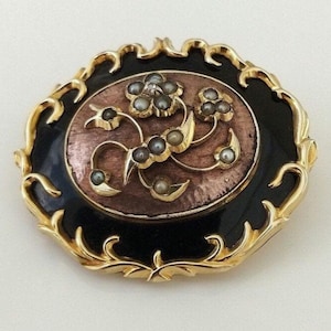 May include: An oval-shaped brooch with a black enamel background and a gold filigree frame. The center features a floral design with a single diamond and pearl accents.