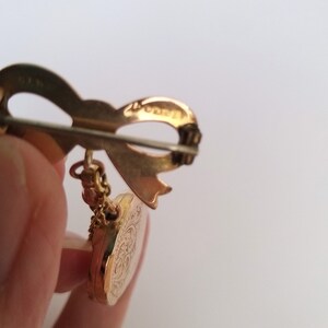 Op de afbeelding: Gouden broche met een strik en een rond medaillon met een bloemmotief. De achterkant van de broche heeft de inscriptie "14K Gold Filled".