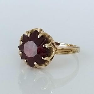 Può includere: Un anello d'oro con una grande pietra preziosa di colore rosso scuro incastonata in un design floreale.