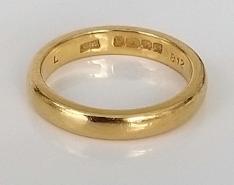 May include: A simple gold wedding band with a smooth finish. The inside of the band is marked with the letters "L" and "812".