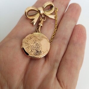 Op de afbeelding: Een gouden medaillon met een delicate strikbedel en een ketting. Het medaillon is gegraveerd met een bloemmotief.
