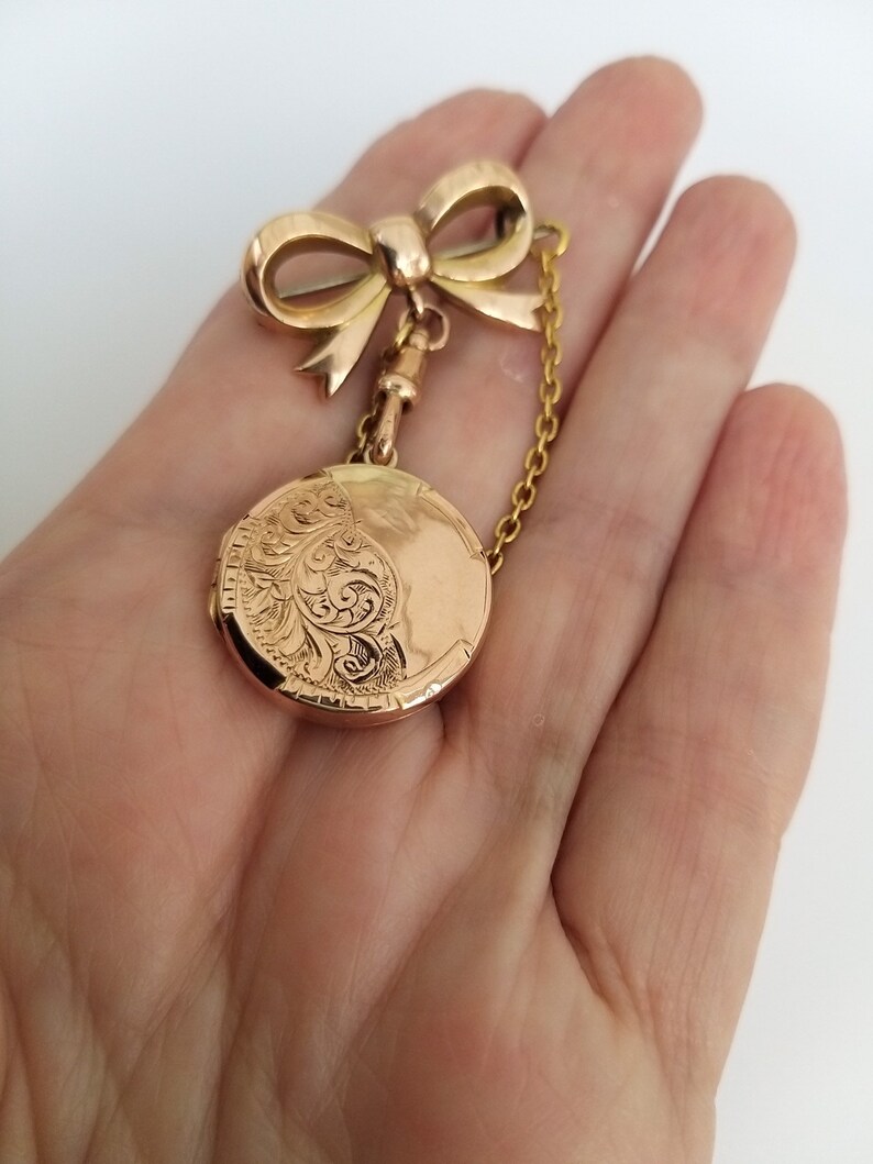 Op de afbeelding: Een gouden medaillon met een delicate strikbedel en een ketting. Het medaillon is gegraveerd met een bloemmotief.