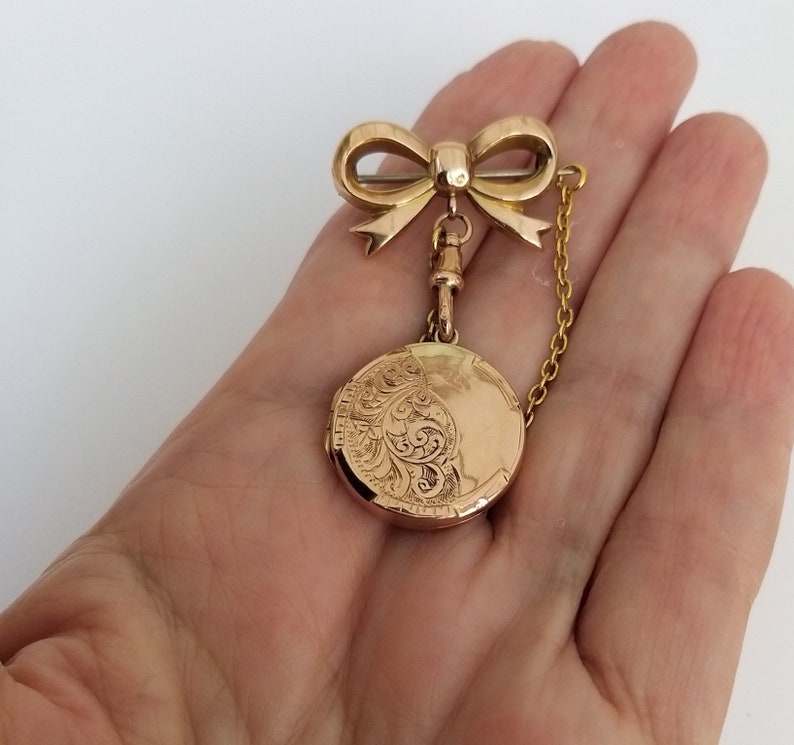 Op de afbeelding: Een gouden medaillon met een delicate strikbedel en een ketting. Het medaillon heeft een ingegraveerd ontwerp.