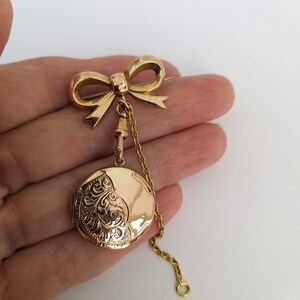 Op de afbeelding: Een gouden medaillon met een strikbedel en een ketting. Het medaillon is gegraveerd met een bloemmotief.