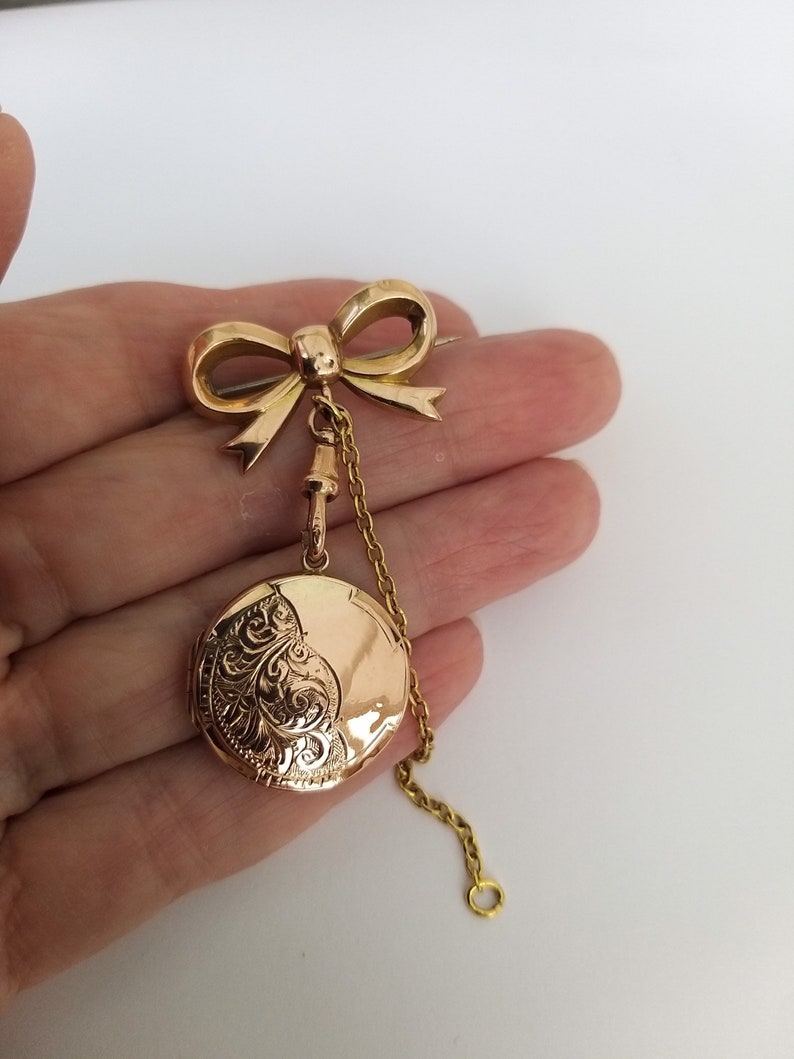 Op de afbeelding: Een gouden medaillon met een strikbedel en een ketting. Het medaillon is gegraveerd met een bloemmotief.