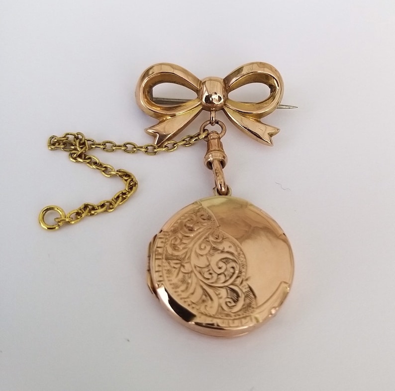 Op de afbeelding: Een gouden medaillon met een delicate strikbedel en een ketting. Het medaillon is gegraveerd met een bloemmotief.