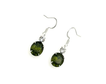 May include: A pair of silver dangle earrings with a large oval green gemstone and a smaller clear rhinestone accent.