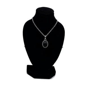 May include: A silver chain necklace with a black oval pendant on a black velvet display stand.