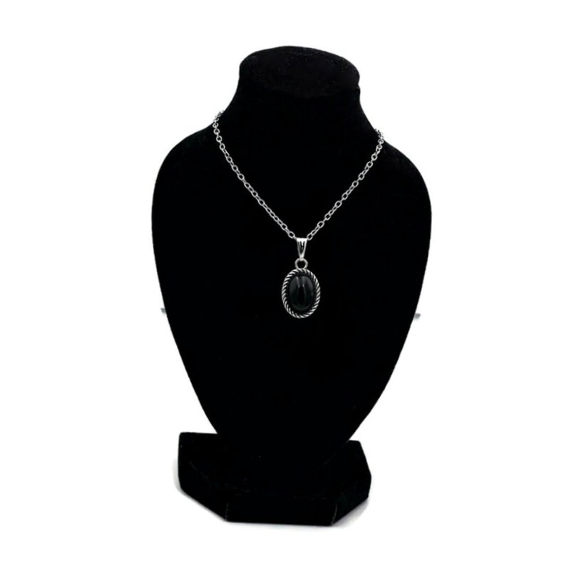 May include: A silver chain necklace with a black oval pendant on a black velvet display stand.