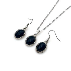 May include: A silver necklace and earrings set with black oval stones. The stones are set in a silver bezel with a decorative border.