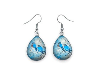 May include: A pair of teardrop-shaped earrings with a silver finish. Each earring features a blue glass cabochon with a painted image of three blue birds perched on a branch with white blossoms.