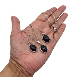 May include: A silver necklace and earrings set with oval-shaped black stones. The stones are set in a silver bezel with a rope-like design around the edge.