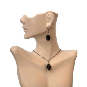 May include: A black oval pendant necklace and matching earrings with a silver-toned metal frame. The necklace has a delicate chain.