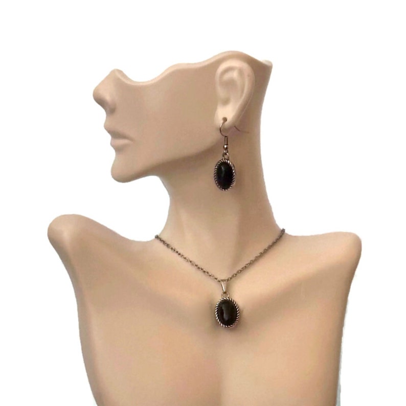 May include: A black oval pendant necklace and matching earrings with a silver-toned metal frame. The necklace has a delicate chain.