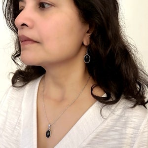 May include: A silver chain necklace and matching earrings with black oval-shaped stones. The stones are set in a silver bezel with a rope-like edge.