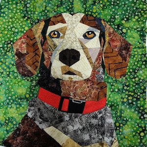 May include: A geometric patchwork dog portrait with a red collar and black buckle. The dog's face features brown, tan, and white patterned fabric, with yellow eyes and a black nose. The background is a green fabric with a spotted pattern.