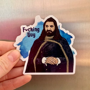Peut inclure: Un autocollant représentant un personnage aux longs cheveux noirs et à la barbe, vêtu d'un manteau sombre à boutons dorés. L'autocollant porte le texte "Fucking Guy" dans une police stylisée, sur un fond bleu aquarelle.