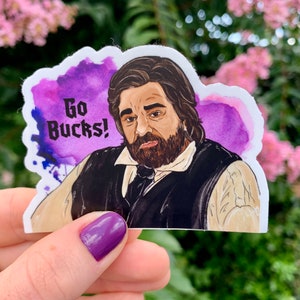 May include: A sticker featuring a watercolor illustration of a man with a beard and the text "Go Bucks!" against a purple and blue watercolor background. The man is wearing a black vest and a white shirt.