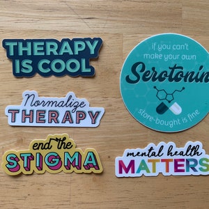 May include: A selection of stickers promoting mental health awareness. The stickers display slogans such as "Therapy is Cool," "Normalise Therapy," and "Mental Health Matters." One sticker is a teal circle with the word "Serotonin" and a chemical structure.