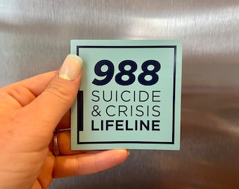 May include: A square sticker with the number "988" in large, dark blue font. Below, the words "SUICIDE & CRISIS LIFELINE" are printed in a smaller, dark blue font. The sticker has a light blue background and a dark blue border.