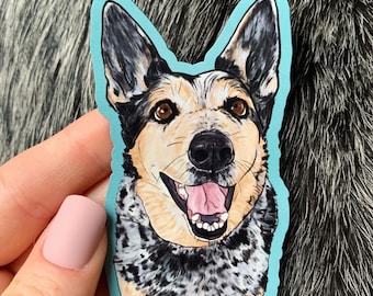 Könnte beinhalten: Ein Aufkleber mit einem lächelnden Hund mit braunen Augen, schwarz-weißem Fell und einer rosa Zunge. Der Aufkleber hat einen hellblauen Rand und ist wahrscheinlich ein Porträt eines Australian Cattle Dog.