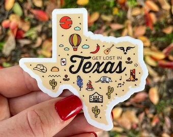 May include: A cream-coloured sticker in the shape of Texas, featuring illustrations of a hot air balloon, guitar, and cactus. The text "Get Lost in Texas" is also included on the sticker.