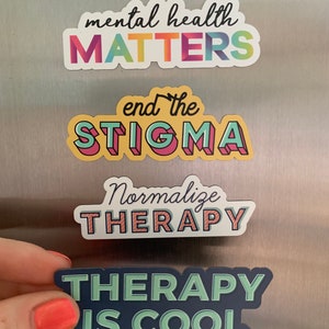 Puede incluir: Una colección de pegatinas coloridas con afirmaciones sobre salud mental. Las pegatinas dicen "mental health MATTERS", "end the STIGMA", "Normalizar TERAPIA" y "THERAPY IS COOL". Las pegatinas son de varios colores, incluyendo rosa, azul, amarillo y verde.