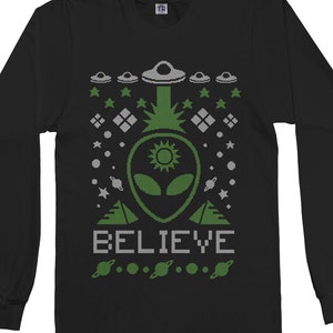 May include: Black long-sleeve shirt with a green alien and the word "BELIEVE" in a pixelated font. The design includes green UFOs, stars, and planets.