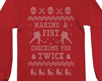 May include: Red long-sleeve t-shirt with a white hockey-themed design. The design features two hockey players, hockey sticks, and the text "Making a Fist Checking You Twice".