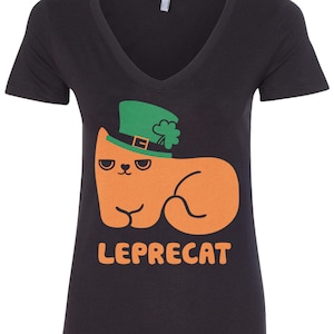 Puede incluir: Camiseta negra de cuello en V con un gato naranja de dibujos animados que lleva un sombrero verde de duende. El texto "LEPRECAT" está impreso debajo del gato.