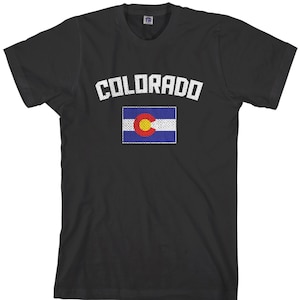 Puede incluir: Camiseta negra con la palabra "COLORADO" en blanco sobre un gráfico de la bandera del estado de Colorado. La bandera presenta un círculo amarillo, un círculo rojo, una franja azul y rayas blancas.