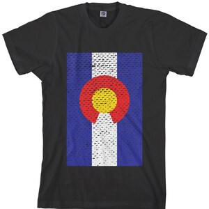 Puede incluir: Camiseta negra con una impresión desgastada de la bandera del estado de Colorado. La bandera presenta un círculo grande con un centro amarillo y un anillo exterior rojo, rodeado de rayas blancas y azules.