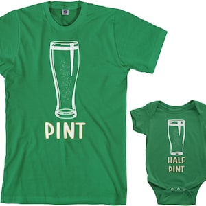 以下が含まれることがあります： 白いアウトラインのピントグラスと黄色の「PINT」の文字が書かれた緑色のTシャツ。白いアウトラインのピントグラスと黄色の「HALF PINT」の文字が書かれた緑色のベビーロンパースとマッチしています。