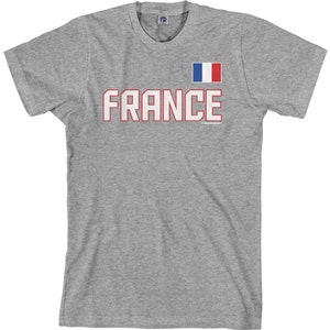 May include: A gray t-shirt with the word "FRANCE" in red with a white outline and a small French flag in the upper right corner.