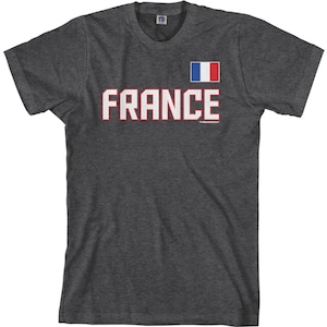 May include: A dark heather grey t-shirt with a white graphic of the word "FRANCE" in bold red letters. A small French flag is displayed above the word.